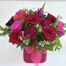 Bouquet of red roses and pink flowers in a magenta vase with ribbon
