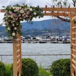 Wooden arbor with cascading blush and cream roses beside a lakeside marina.