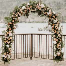 Large floral arch of peach and white blooms on a deck overlooking the water