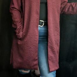 Person wearing a burgundy long coat over a black top and jeans