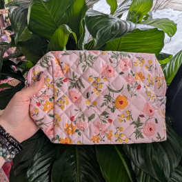 Pink floral quilted pouch held in front of large green houseplant leaves