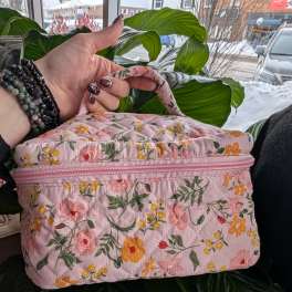 Pink floral quilted zippered bag held in front of a large green plant