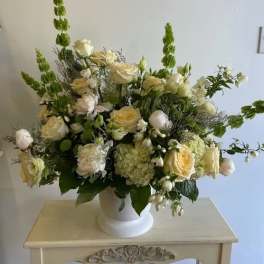 Cream and white floral arrangement in a white pedestal vase