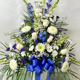 Tall white and blue floral arrangement with a blue ribbon in a vase