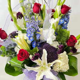 Tall bouquet of red roses, white lilies, and blue flowers with lavender ribbon
