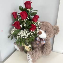 Red roses in a glass vase beside a teddy bear