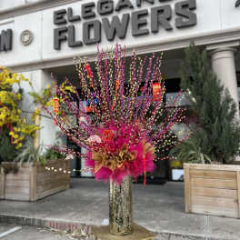 Tall pink and gold floral arrangement in a vase outside a flower shop
