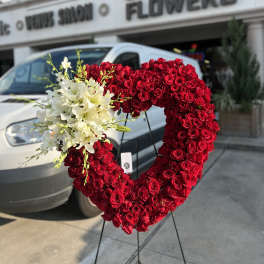 Heart-shaped red rose arrangement with white lilies on a stand