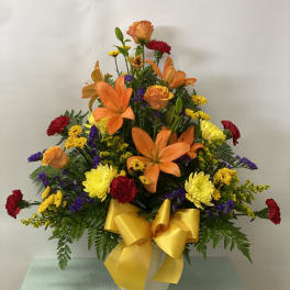 Colorful flower arrangement with orange lilies, yellow and red blooms, and a yellow bow