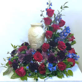 Red roses and blue flowers arranged around a cream vase