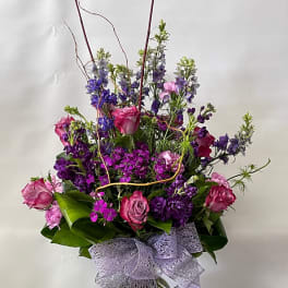 Tall bouquet of pink and purple flowers in a glass vase with a lavender bow