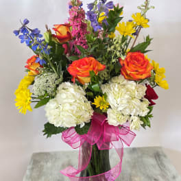 Mixed bouquet of roses, hydrangeas, and daisies in a glass vase with a pink ribbon