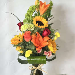 Tall mixed bouquet in a dark glass vase with sunflowers, lilies, and roses