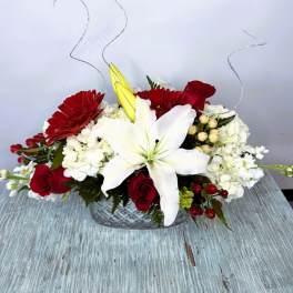 Red and white floral arrangement with a large white lily in a glass bowl