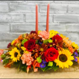Low floral centerpiece with two orange taper candles and mixed blooms