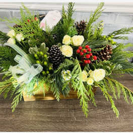 Holiday floral arrangement with cream roses, pinecones, and evergreen branches in a wooden box