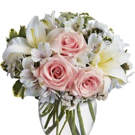 Small arrangement of pale pink roses and white lilies in a clear glass vase.