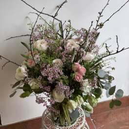 Tall bouquet of white and pink flowers with branching twigs in a glass vase