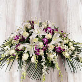 White lilies, roses, and purple orchids arranged in a low spray.