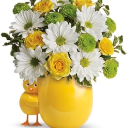 Yellow vase with daisies and roses, with a small chick figurine beside it