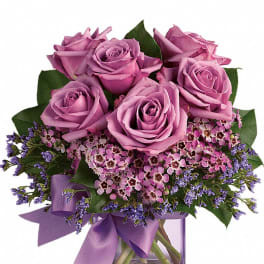 Lavender roses and pink filler flowers in a purple glass cube vase with matching ribbon.