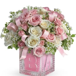 Pink and white roses arranged in a glass cube vase with pink ribbons
