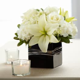 Low white lily and rose arrangement in a black square vase with votive candles