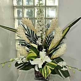 Tall white floral arrangement in a square vase with large tropical leaves
