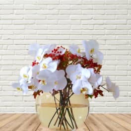 White orchid arrangement in a round glass vase with red berry accents