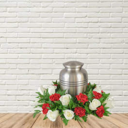 White roses and red carnations arranged around a silver urn.