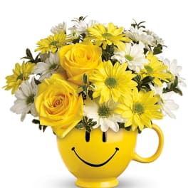 Yellow and white daisies with yellow roses arranged in a yellow smiley-face mug.