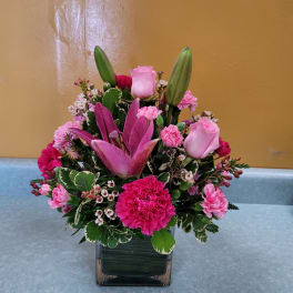 Pink lilies and roses arranged in a square glass vase