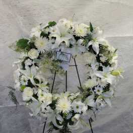 White floral wreath on a black stand with lilies and daisies