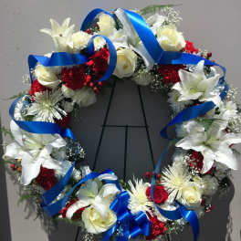Circular wreath of white lilies, roses, and red carnations with blue ribbon