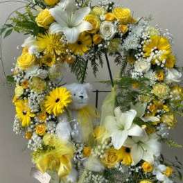 Yellow and white floral wreath on a stand with a teddy bear in the center