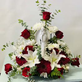 Sympathy floral arrangement with red roses, white lilies, and a Virgin Mary figurine