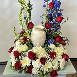 Red roses, white blooms, and blue delphinium around a white vase