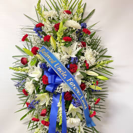 Standing funeral spray with red, white, and blue flowers and a blue ribbon