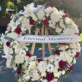 Large funeral wreath of white flowers with red roses and a memorial ribbon
