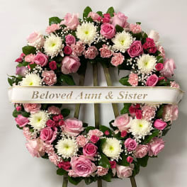 Pink and white floral funeral wreath on an easel with a memorial ribbon