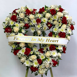 Heart-shaped floral wreath with red and white roses and daisies on an easel