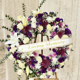 Circular sympathy wreath of white, purple, and pink flowers on an easel