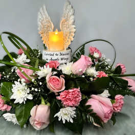 Pink roses and carnations arranged around a lit candle with angel wings