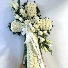White funeral standing cross with lilies, roses, and carnations on an easel