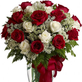 Red and white roses arranged in a clear glass vase with a red ribbon