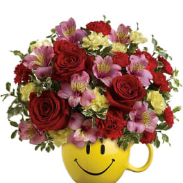 Bouquet of red roses, pink alstroemeria, and yellow carnations in a smiley-face mug