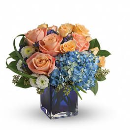Peach roses and blue hydrangeas in a square glass vase