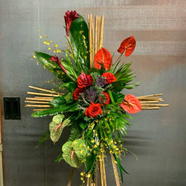 Tall tropical floral arrangement with red anthuriums and roses on a bamboo stand