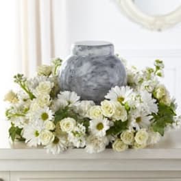 White daisies and cream roses arranged around a gray urn