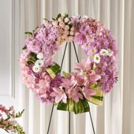Pink floral wreath on a black stand with ribbon accents